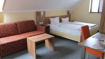 A small, cozy room with a bed, a sofa, a table, and a chair.