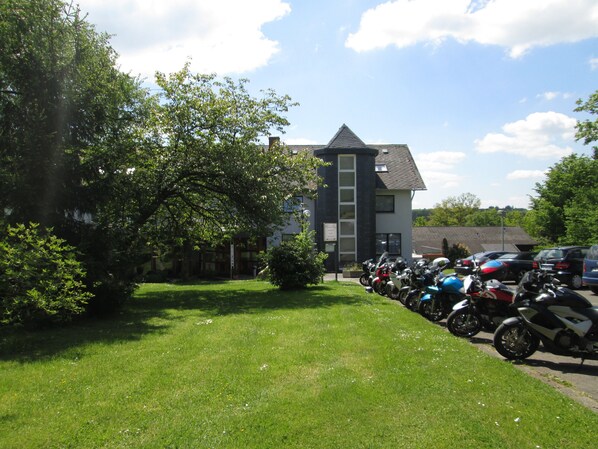 A grassy area with a row of parked motorcycles and a building with a modern design in the background. - Landhotel Karrenberg (Kirchberg)