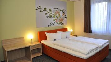 A hotel room with a single bed, two bedside tables, a nightstand, a wall-mounted painting, and a window with curtains.