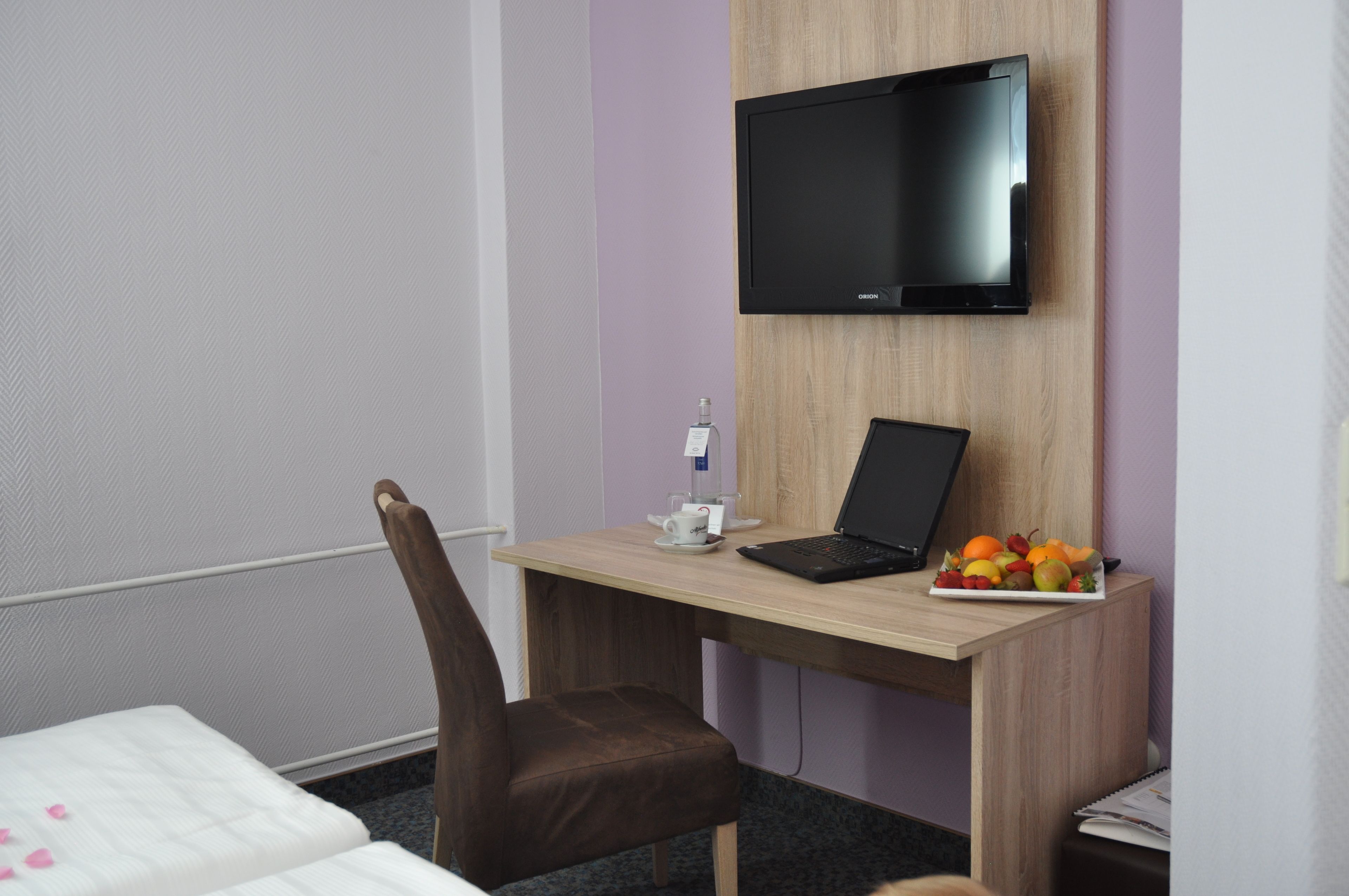Ein Hotelzimmer mit einem Bett, einem Schreibtisch mit Laptop, einem Fernseher und einer Obstplatte.