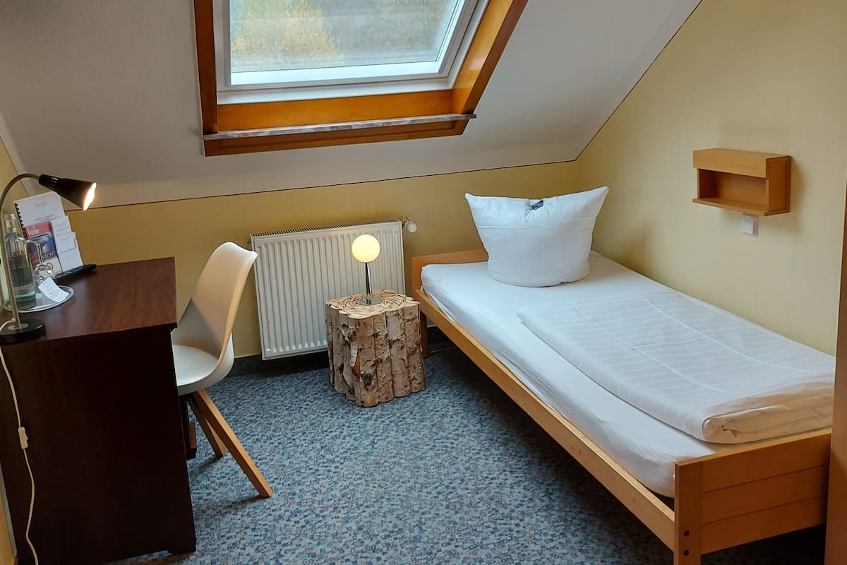 Een kleine, driehoekige slaapkamer op zolder met een dakraam, een enkel bed, een bureau met stoel en een radiator.