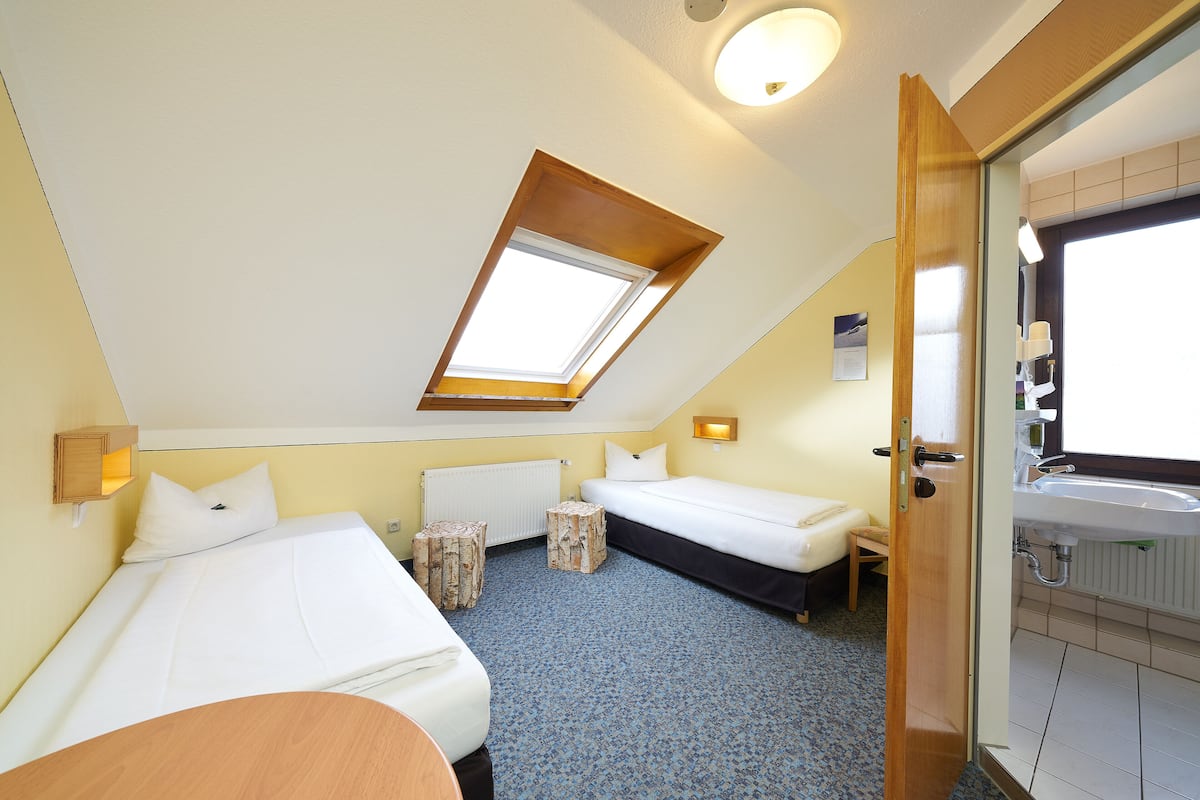 Een kamer met twee bedden, een dakraam, een badkamer met een wastafel en een klein tafeltje.