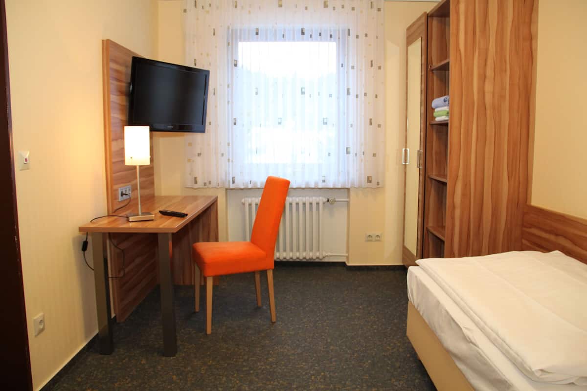 Een hotelkamer met een houten bureau, een stoel, een bed, een aan de muur bevestigde televisie en een raam met gordijnen.