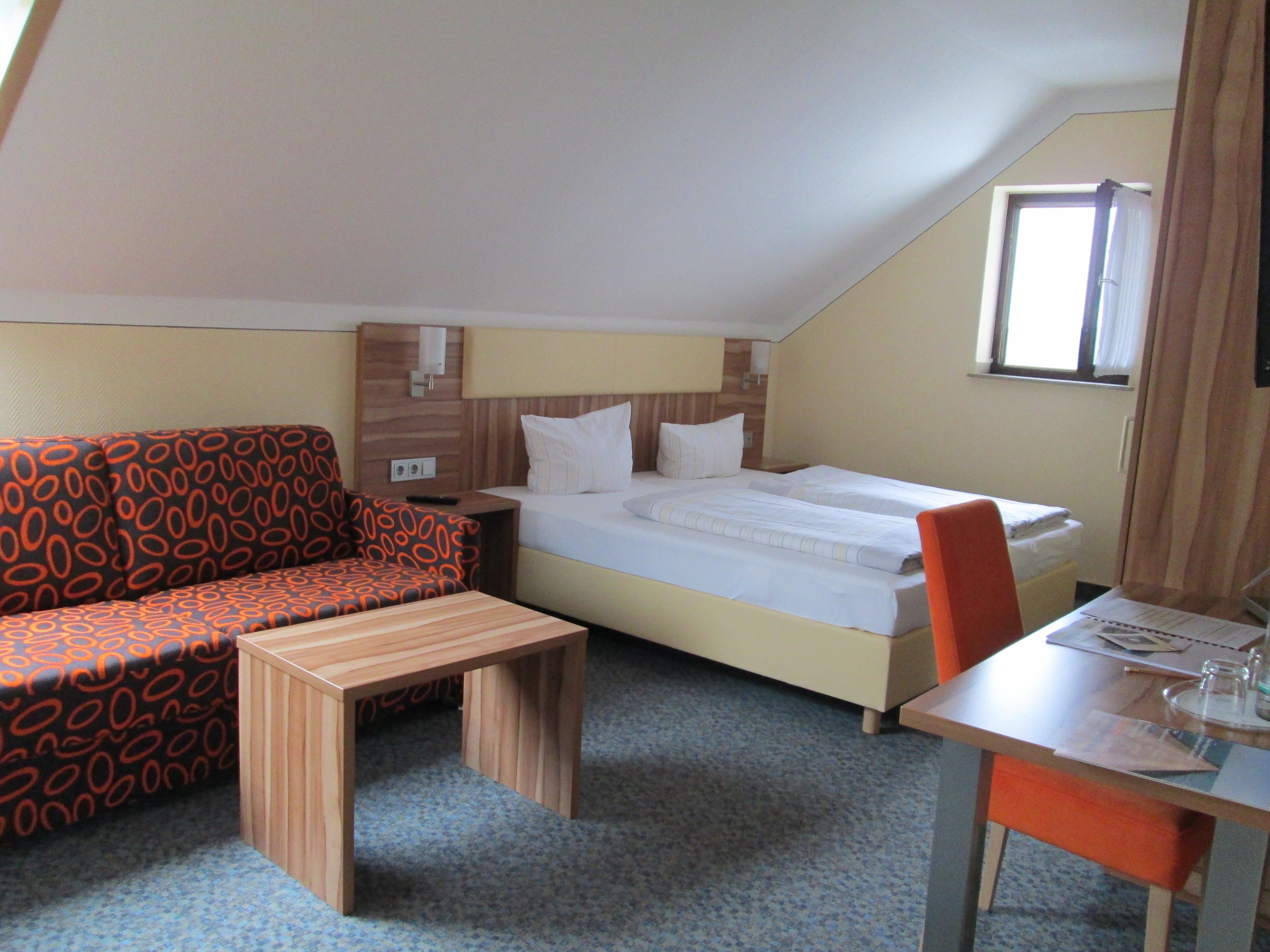 A small, cozy room with a bed, a sofa, a table, and a chair.