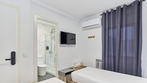 Een hotelkamer met douche, toilet, bed, nachtkastje en een aan de muur bevestigde televisie.