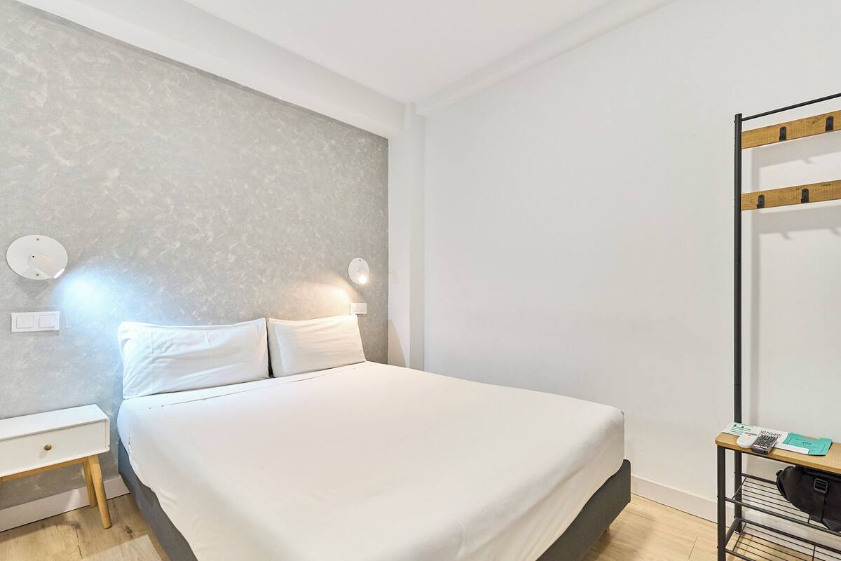 Une chambre d’hôtel bien rangée, avec un lit, des tables de chevet, une lampe fixée au mur et un miroir.