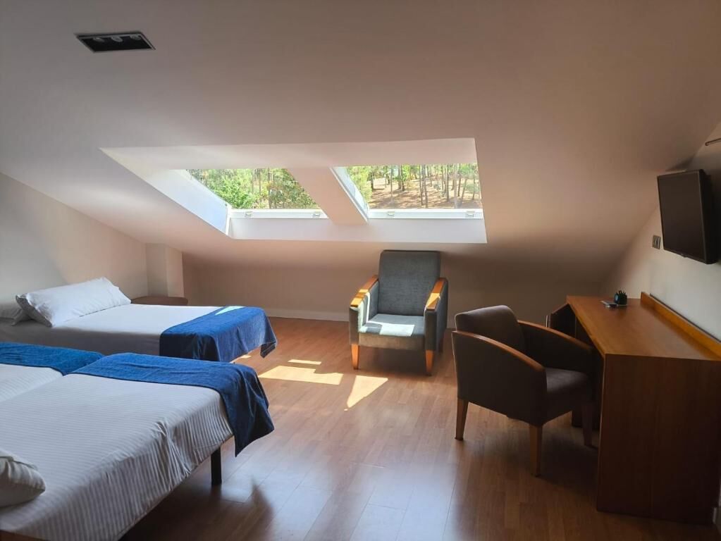 Une chambre avec deux lits, un bureau, une chaise et une fenêtre de toit.
