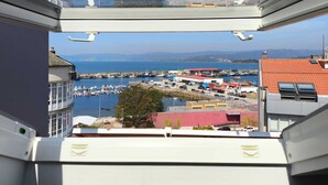 Blick von einem Balkon auf eine Marina mit Booten, Gebäuden und einer fernen Bergkette.