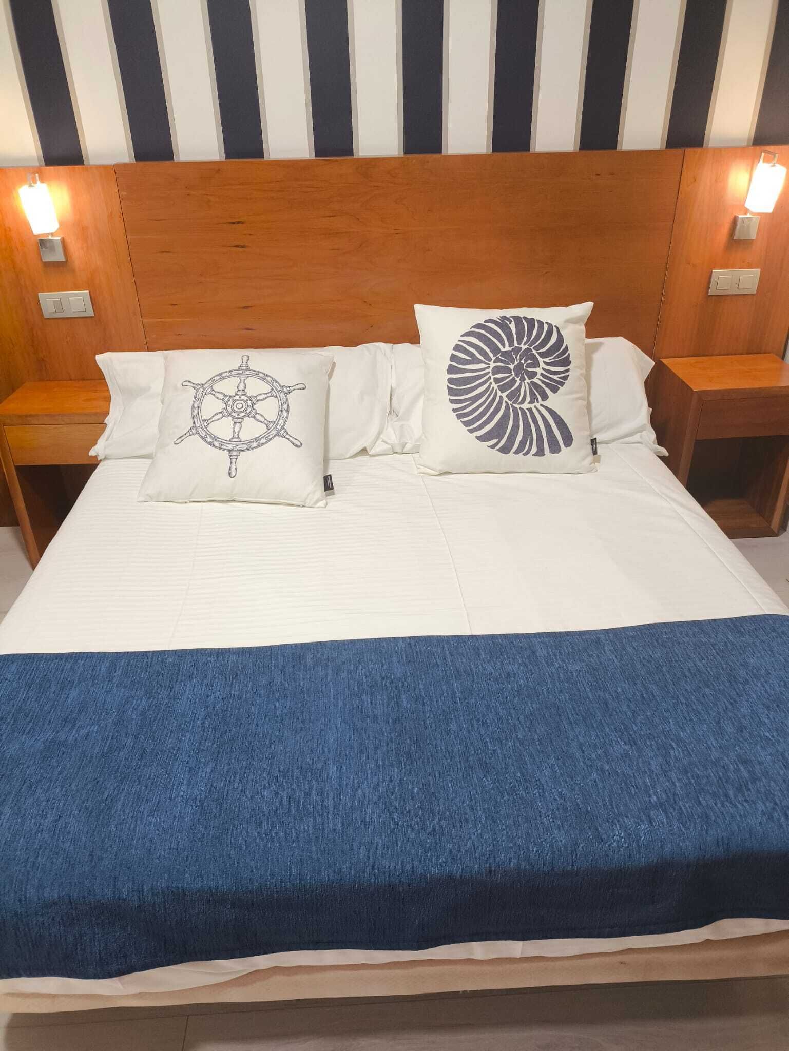 Ein Bett mit blauer Decke, zwei Kissen mit Meeresmotiven, einem Holz-Kopfschild und Nachttischlampen.