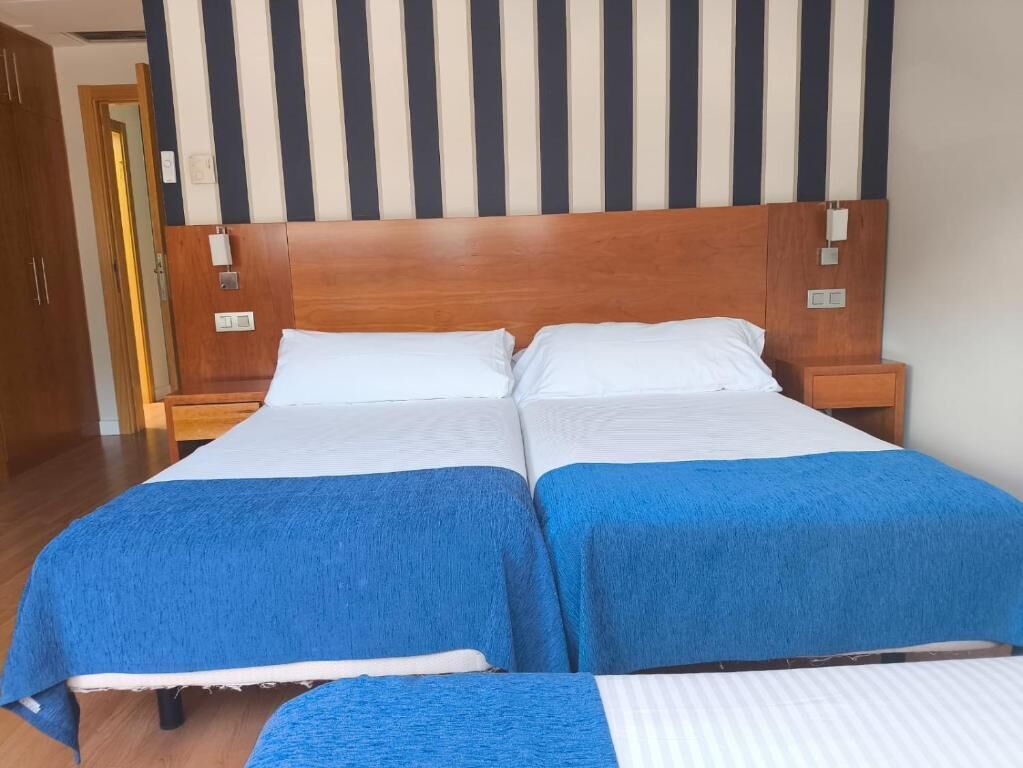 A double bed with a wooden headboard, two bedside tables, and a striped wall behind.