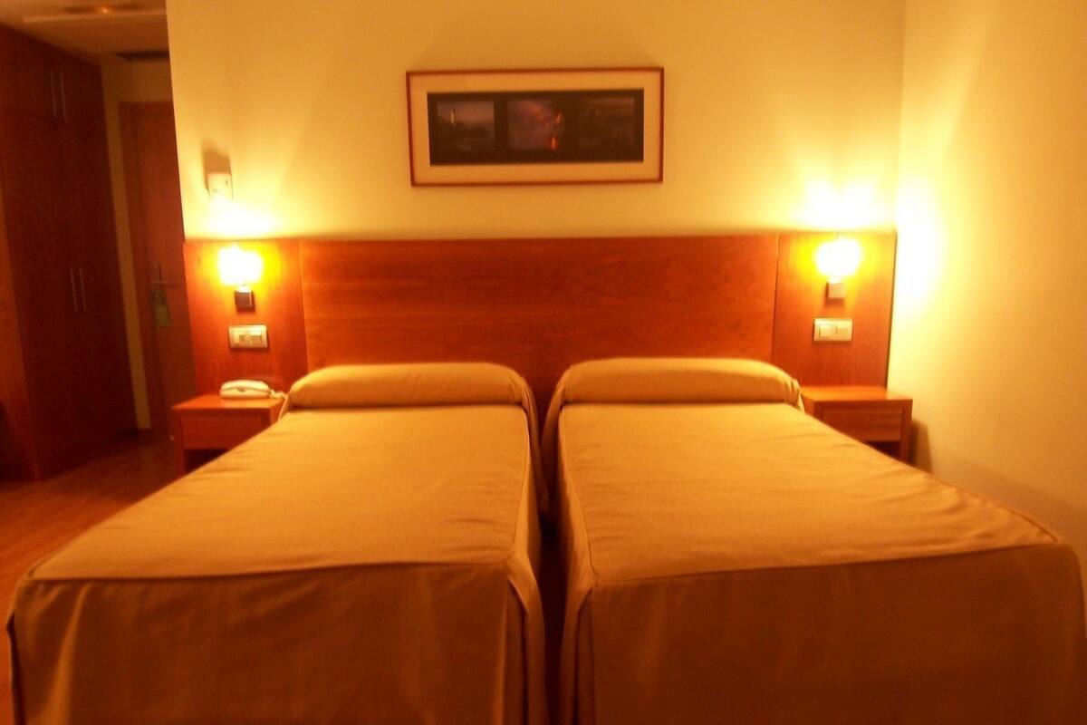 A hotel room with two beds, wooden headboard, bedside lamps, and a framed picture on the wall.