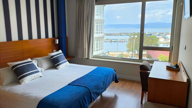 Ein Hotelzimmer mit einem großen Bett, einem Schreibtisch und Blick auf einen Yachthafen und Gebäude am Wasser.