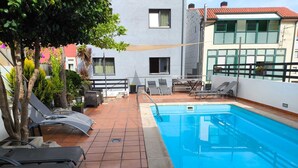 Ein Pool auf dem Dach mit Liegestühlen, einem Tisch und Topfpflanzen.