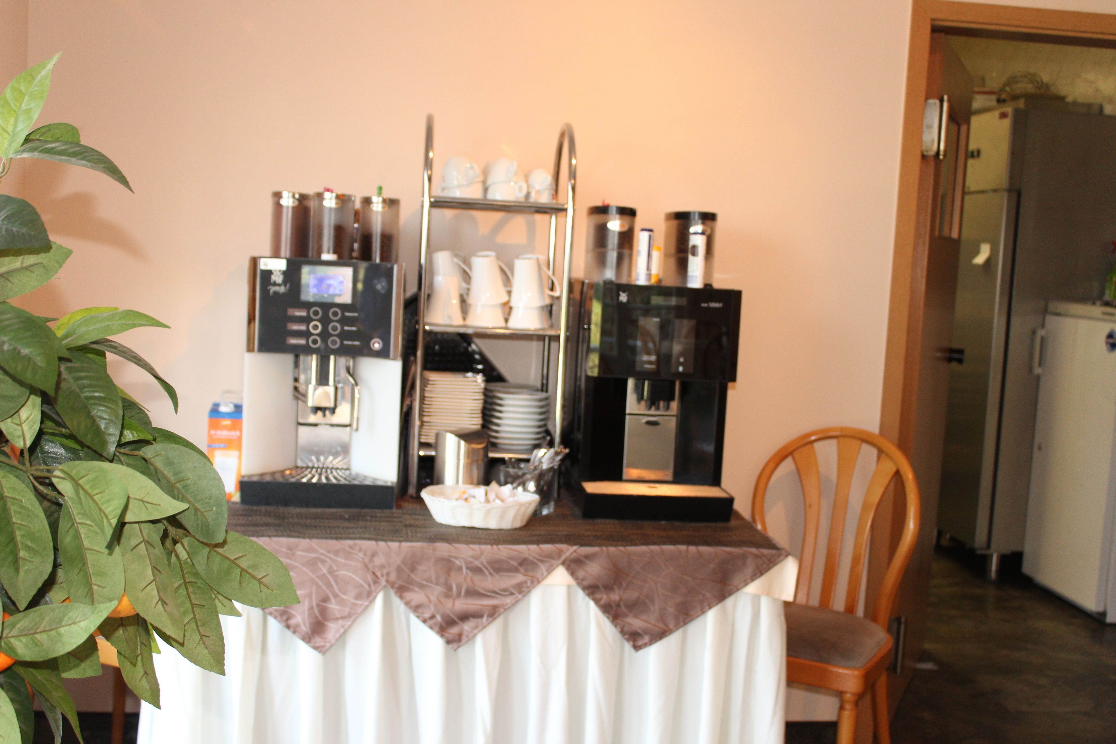 A kitchenette with a coffee machine, a tea dispenser, and a shelf with cups and plates.
