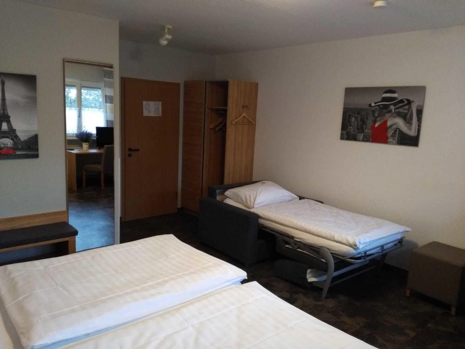 A small, compact room with two single beds, a desk, and a wardrobe.