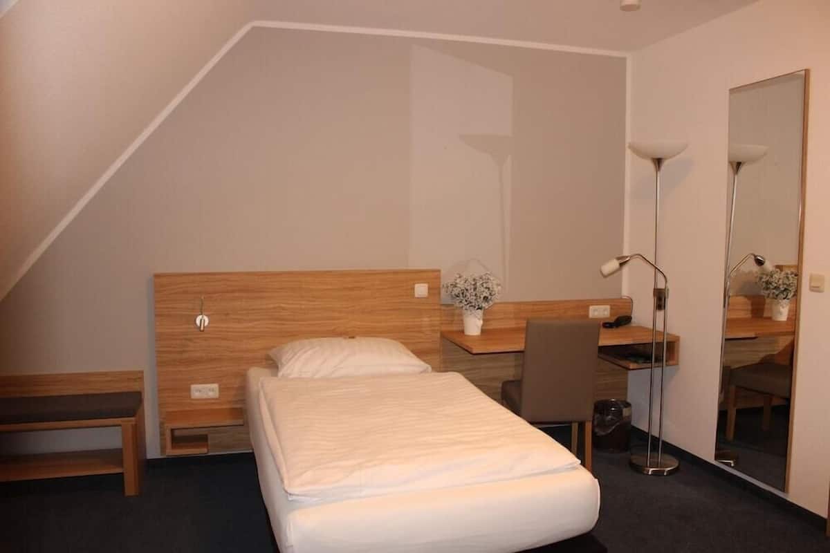 A bedroom with a bed, a desk, a chair, a lamp, and a mirror.