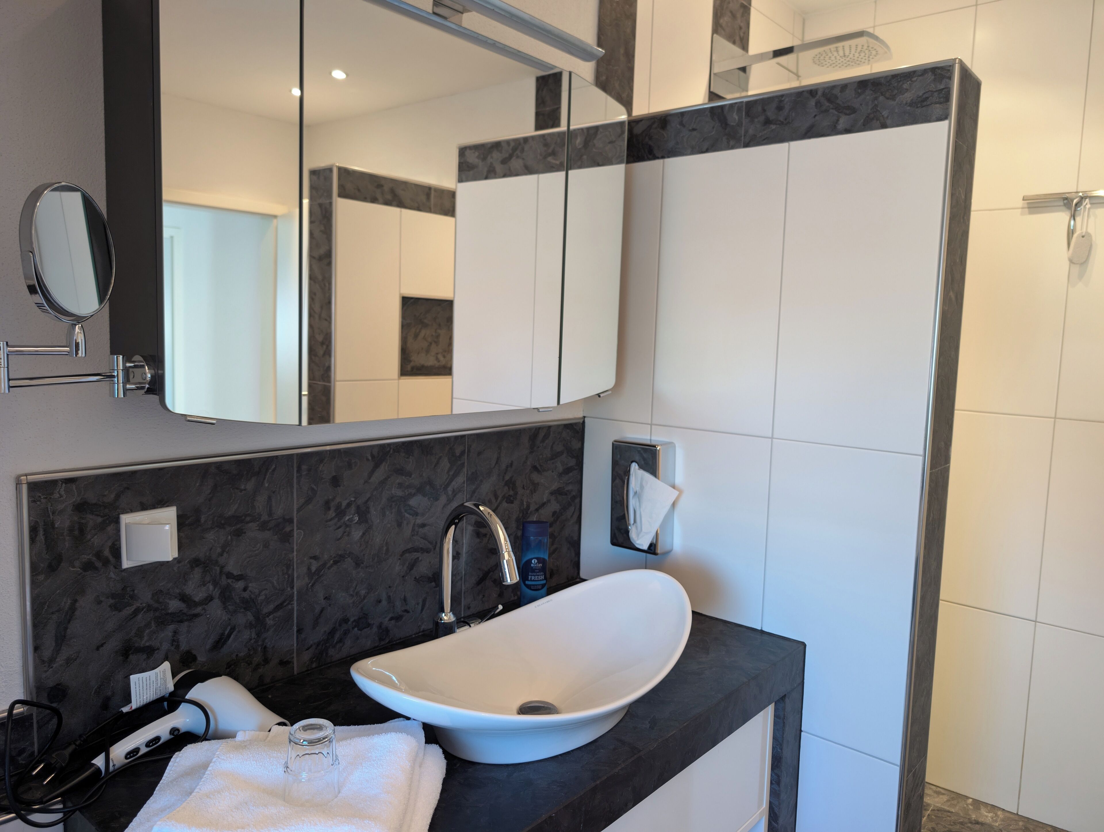 A modern bathroom with a white sink, dark marble countertop, and a large mirror.