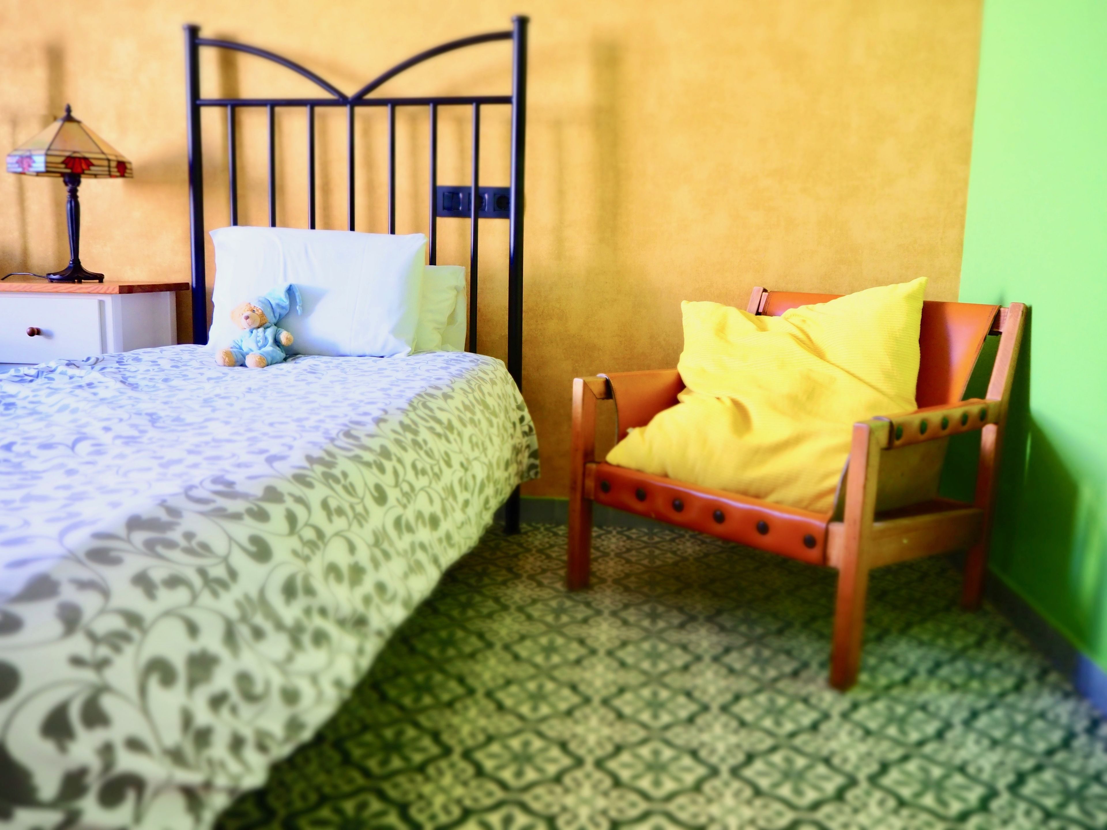 Une chambre à coucher avec un lit, une table de chevet, une lampe, une chaise et un sol à motifs.