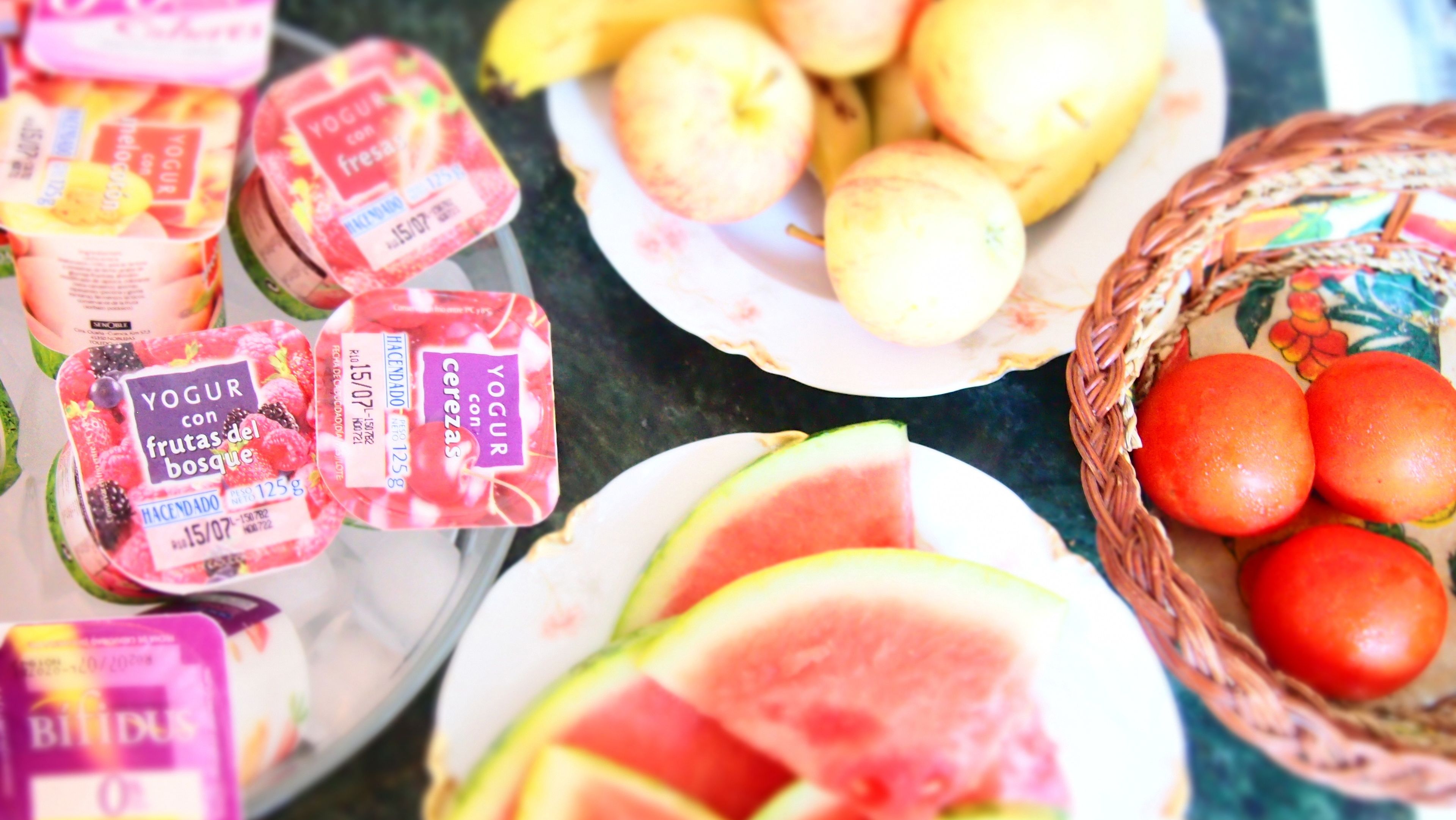 A table with various food items including yogurt, fruits, and a basket of tomatoes.