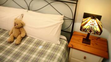 Una cama con una colcha escocesa, un almohilar blanco y un oso de peluche a la izquierda. Junto a la cama, una mesita de noche con una lámpara de vitral.
