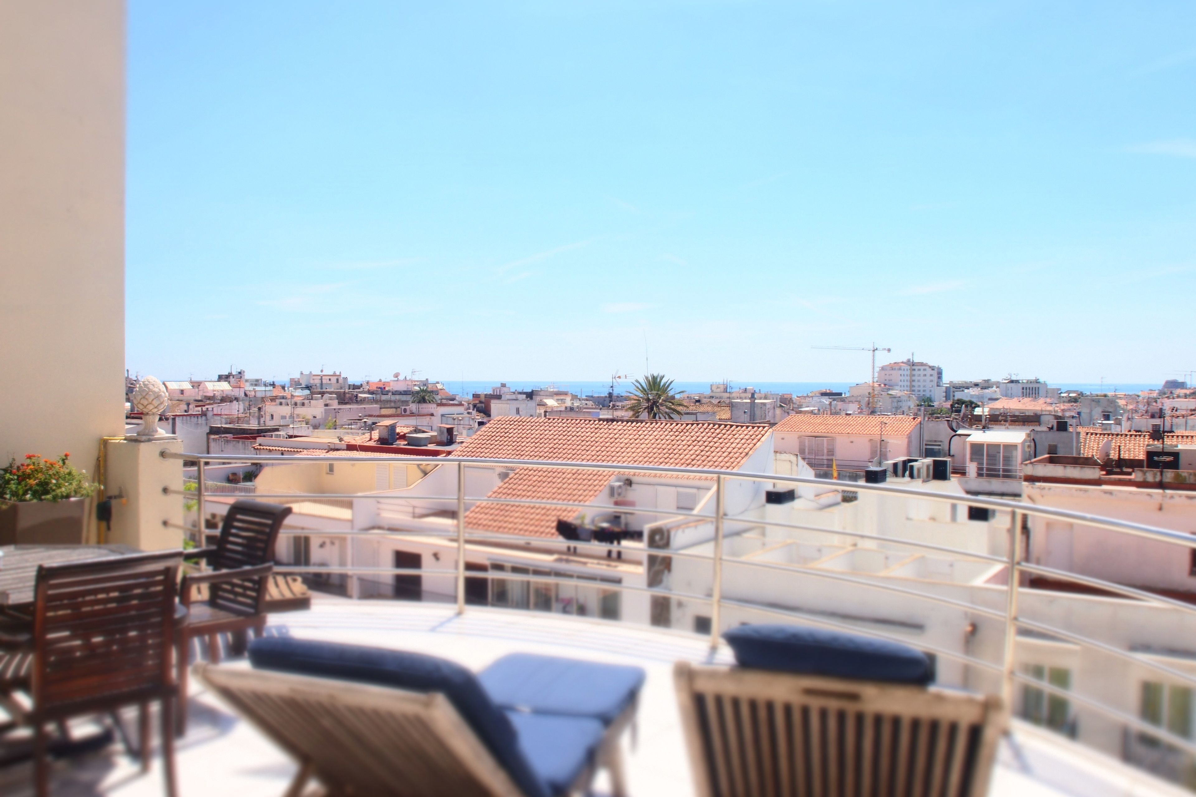 Un balcón con sillones de descanso y una mesa, con vista a un paisaje urbano de edificios y cielo despejado.