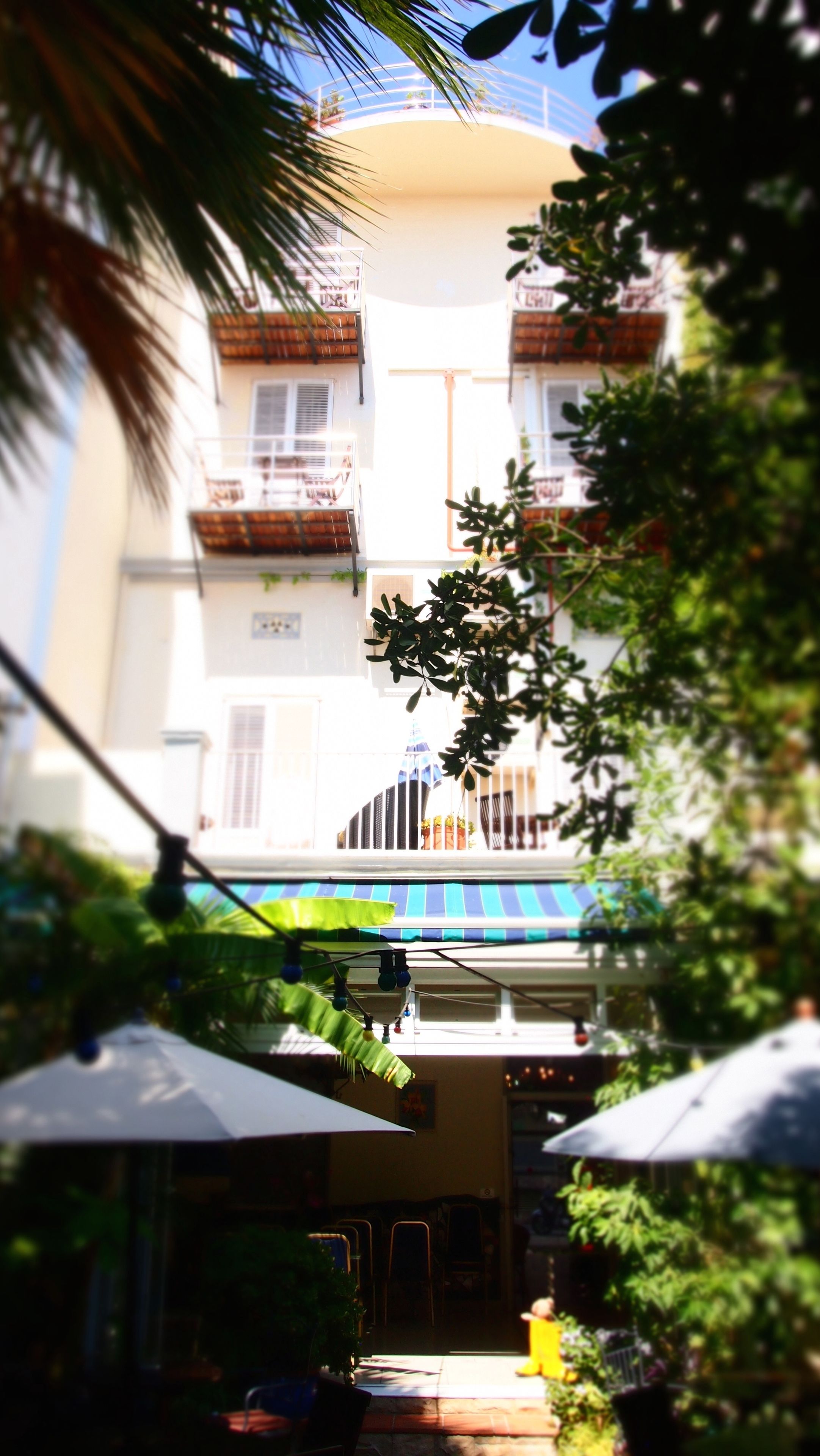Un edificio de varios pisos con balcones, mobiliario exterior y una zona cubierta con sombrillas.