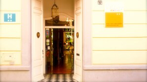 Entrada de hotel con suelo a cuadros, un farol colgante y un cartel que indica el bar y el jardín.