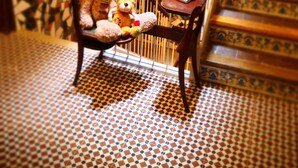 Una escalera con piso estampado, una silla de madera con un osito de peluche, y una mesita con un libro.