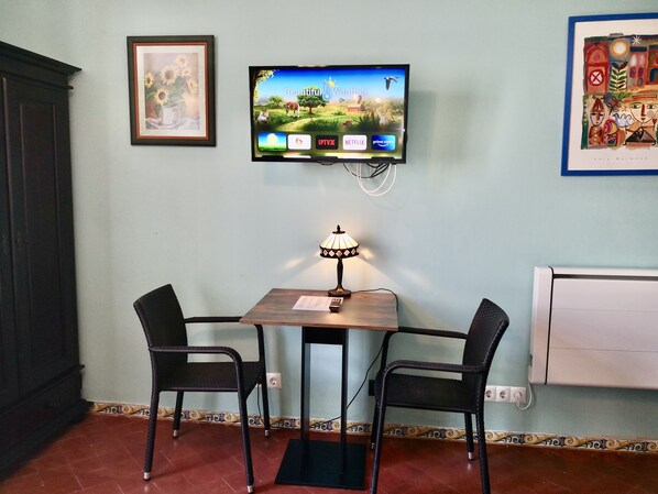 Un pequeño comedor con una mesa y dos sillas, un televisor montado en la pared y un cuadro enmarcado sobre el televisor.