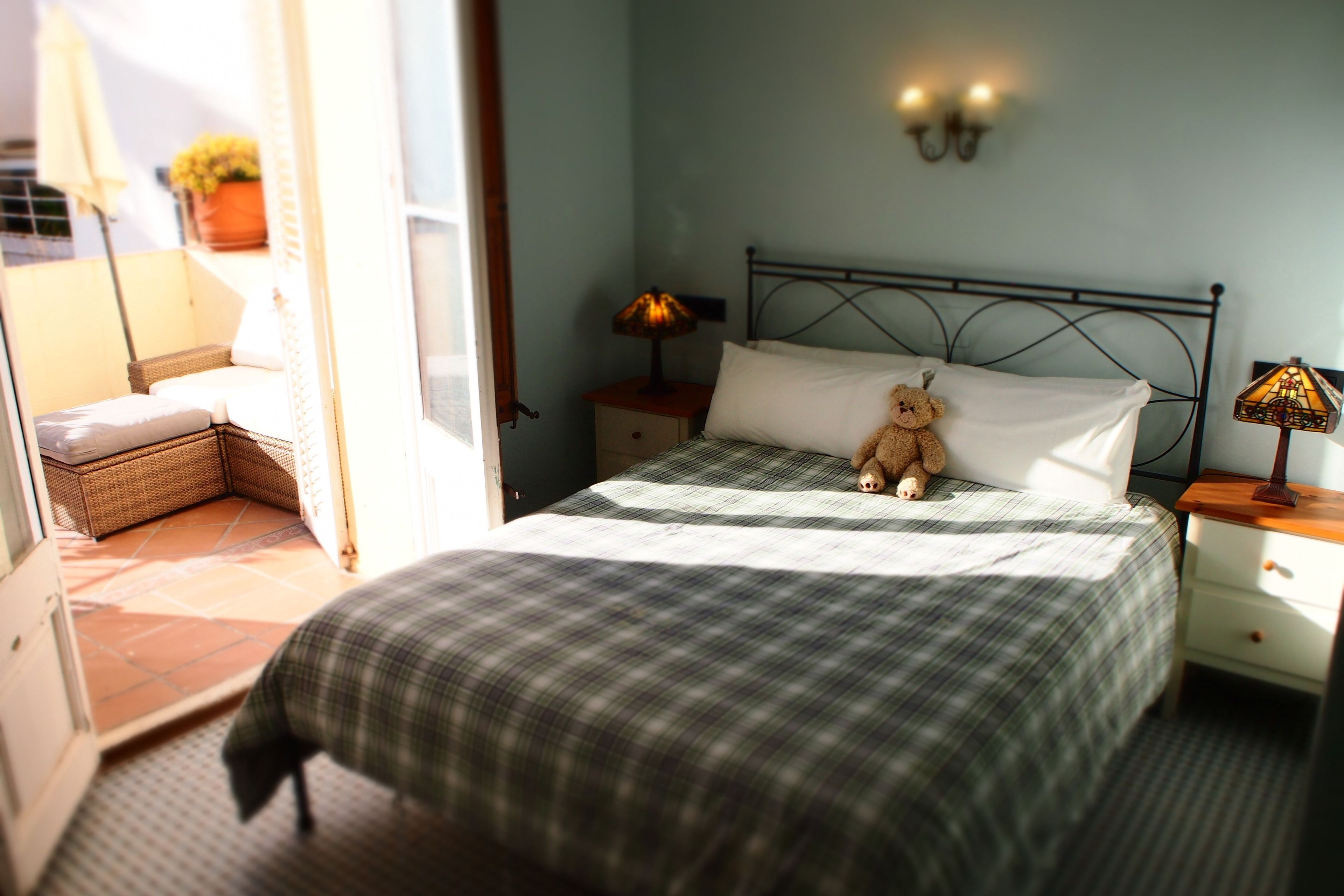 A bedroom with a bed, a bedside lamp, a nightstand, a teddy bear, and a view of the outside balcony.