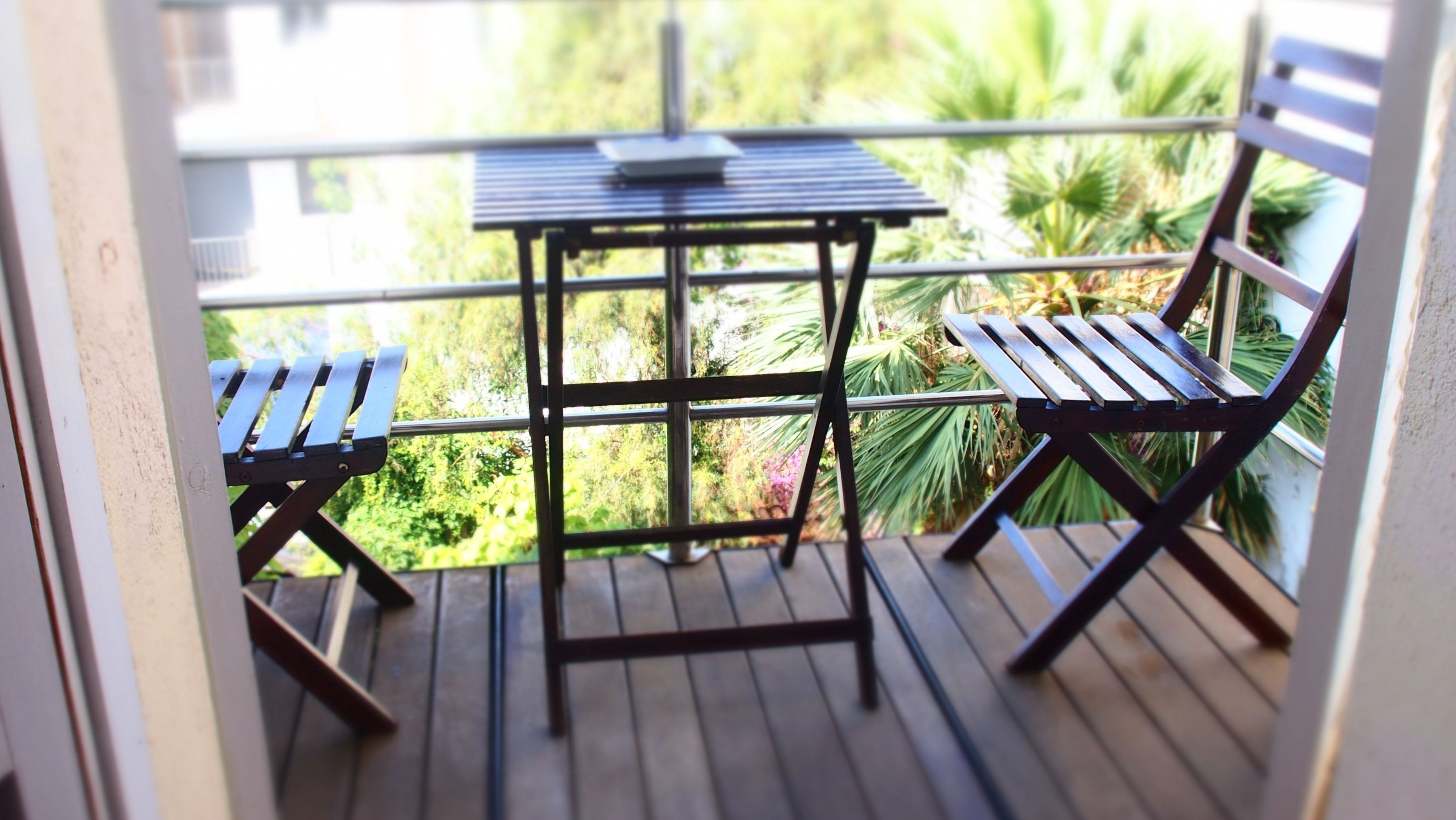 Un balcon avec une petite table et deux chaises, donnant sur un jardin où poussent différentes espèces de plantes.