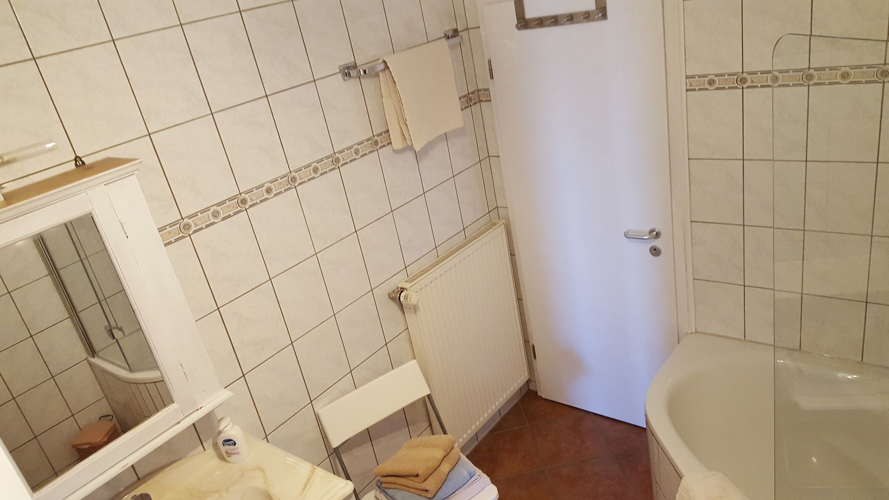 Ein Badezimmer mit einer weißen Badewanne, einem Waschbecken inklusive Spiegel und einem Handtuchhalter.