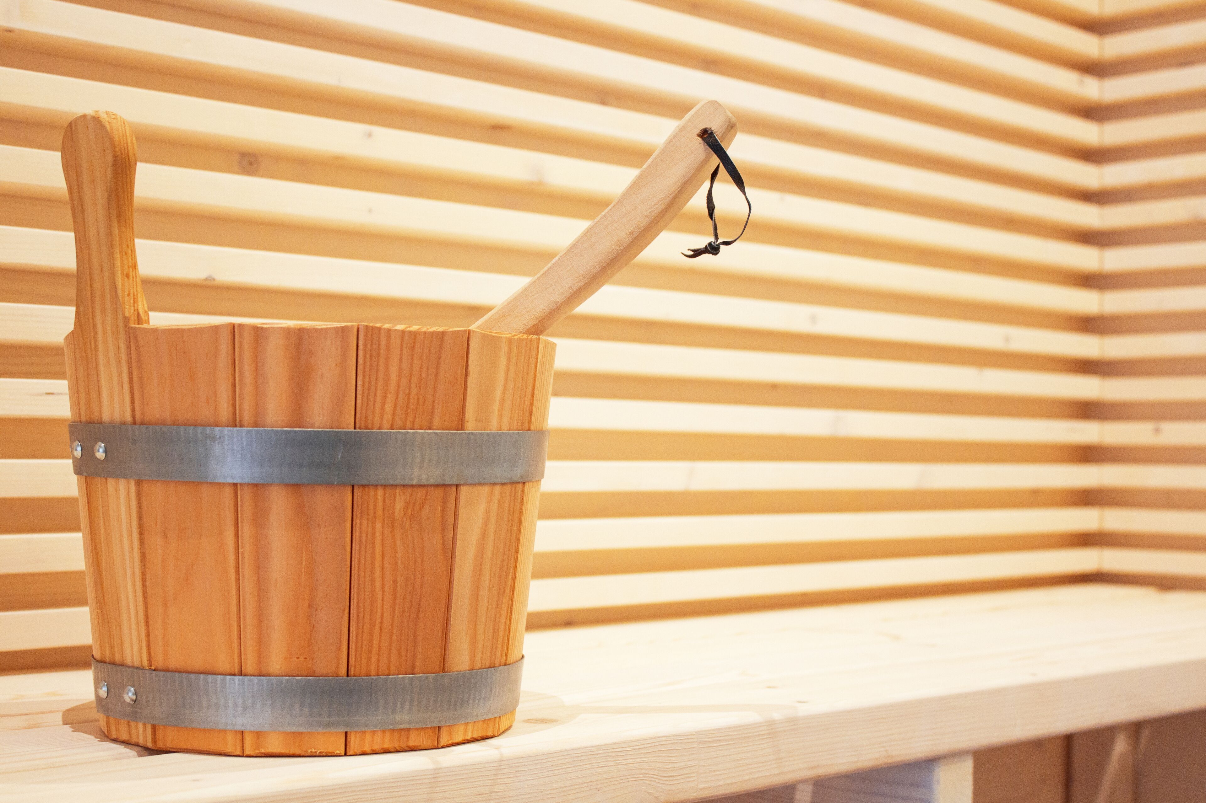 A wooden bucket with a metal handle and strap, placed on a wooden shelf.