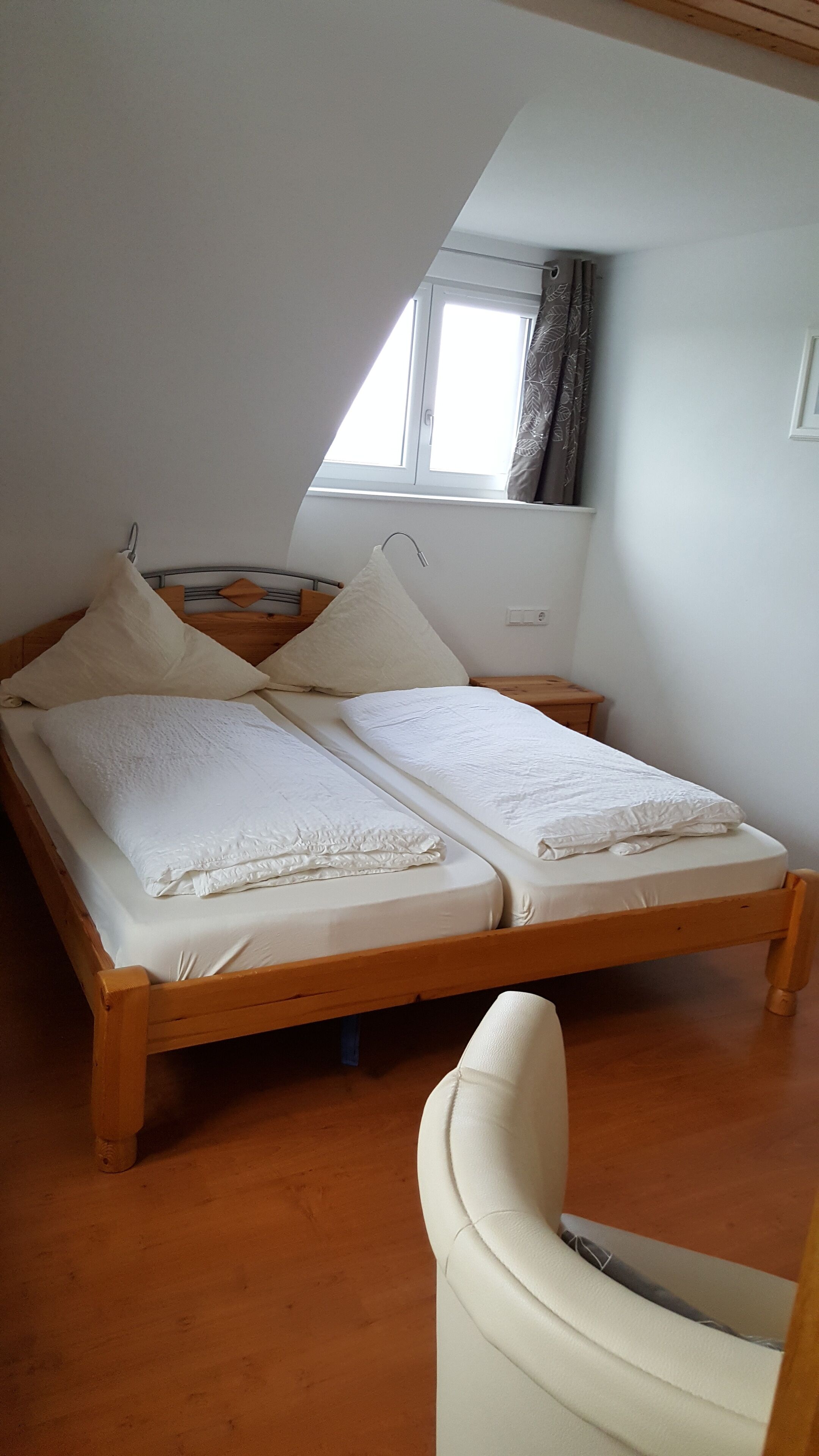 Een eenpersoonsbed met twee kussens en een witte deken in een kamer met houten vloer en een schuine plafond.