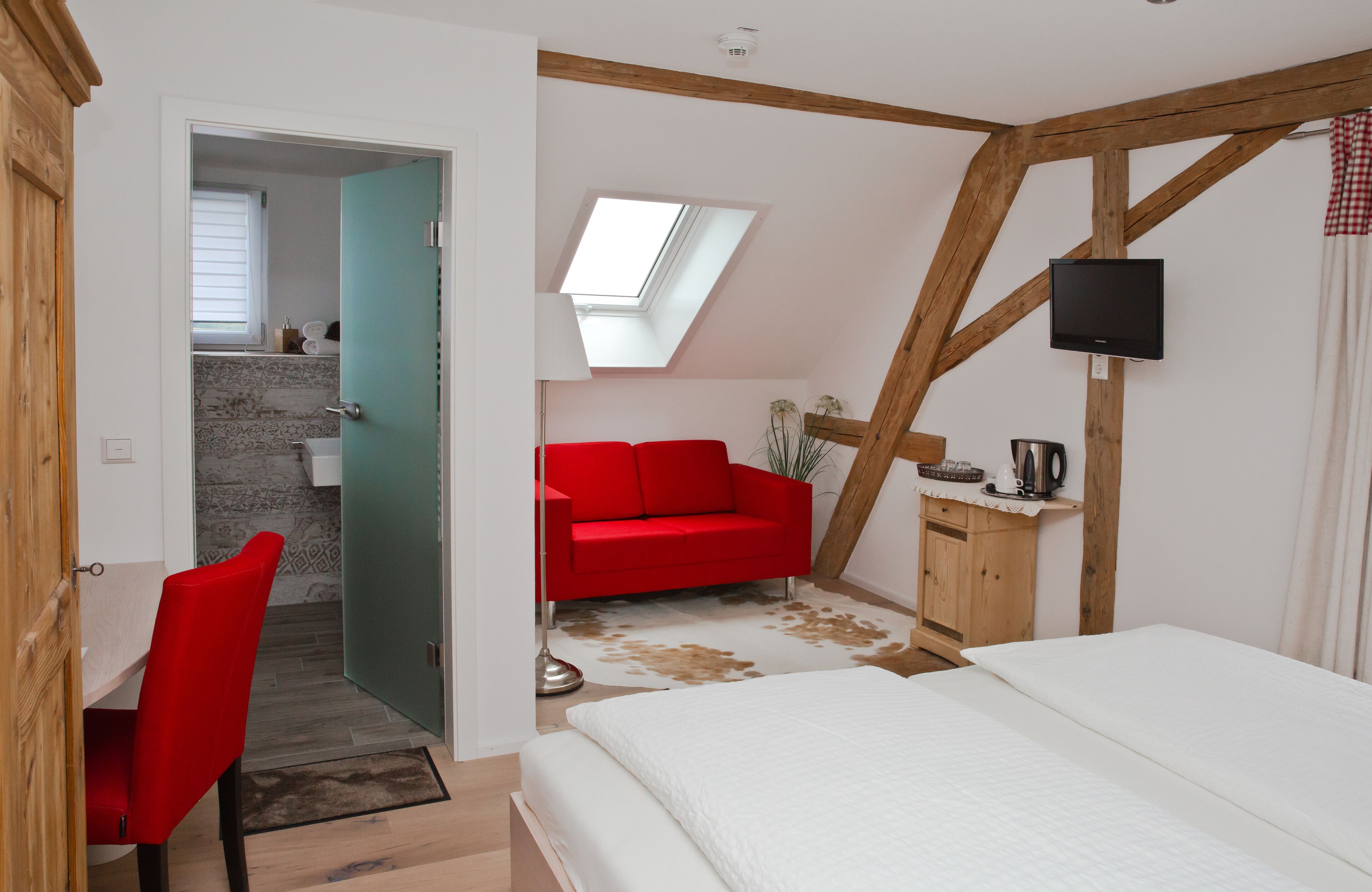 Una camera da letto con un letto, un divano rosso, un armadio in legno, una televisione e un lucernario.