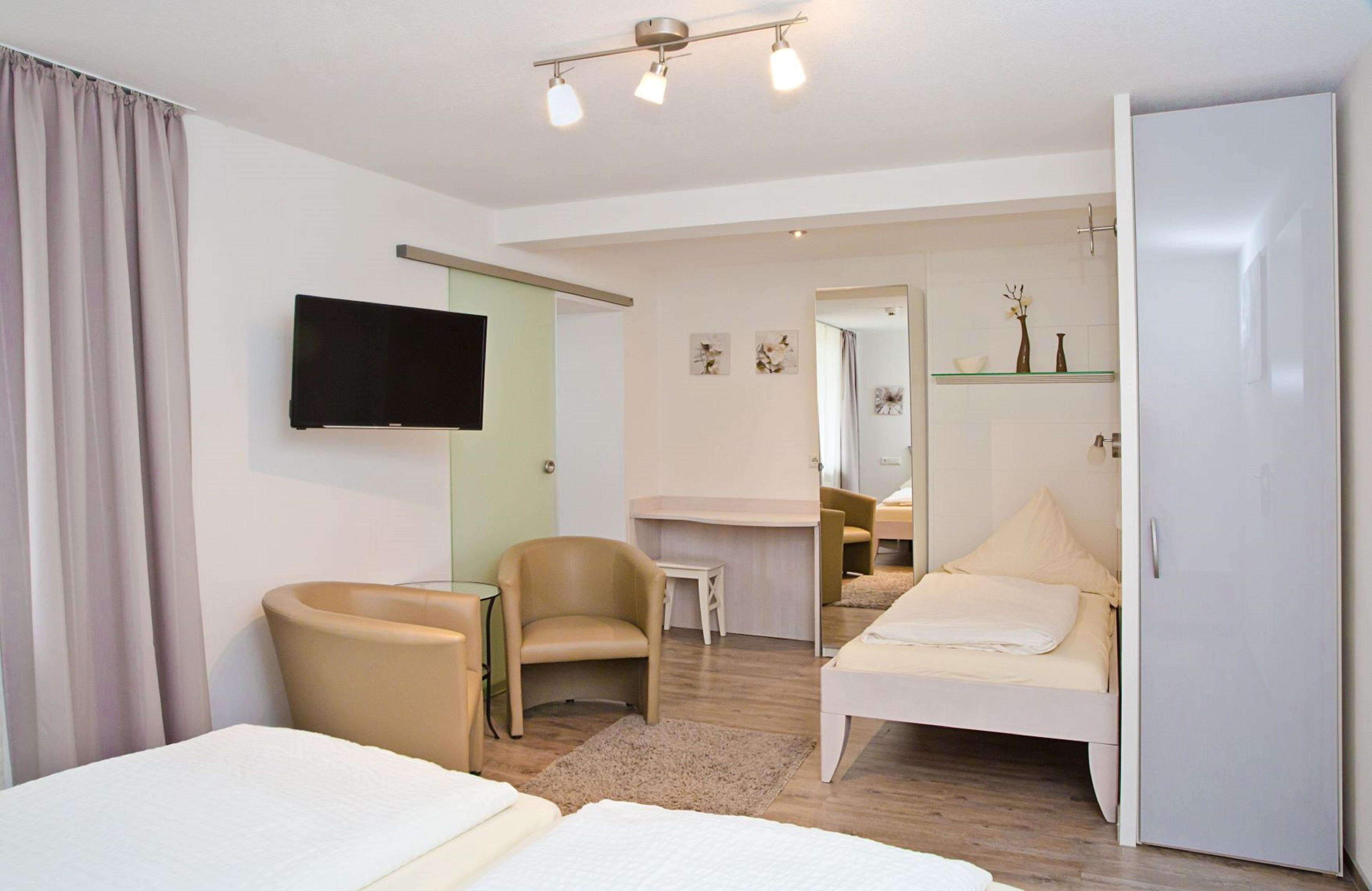 Quarto de hotel moderno com cama, poltrona, escrivaninha, televisão e espelho.