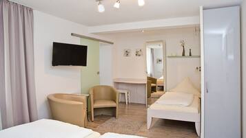 Quarto de hotel moderno com cama, poltrona, escrivaninha, televisão e espelho.