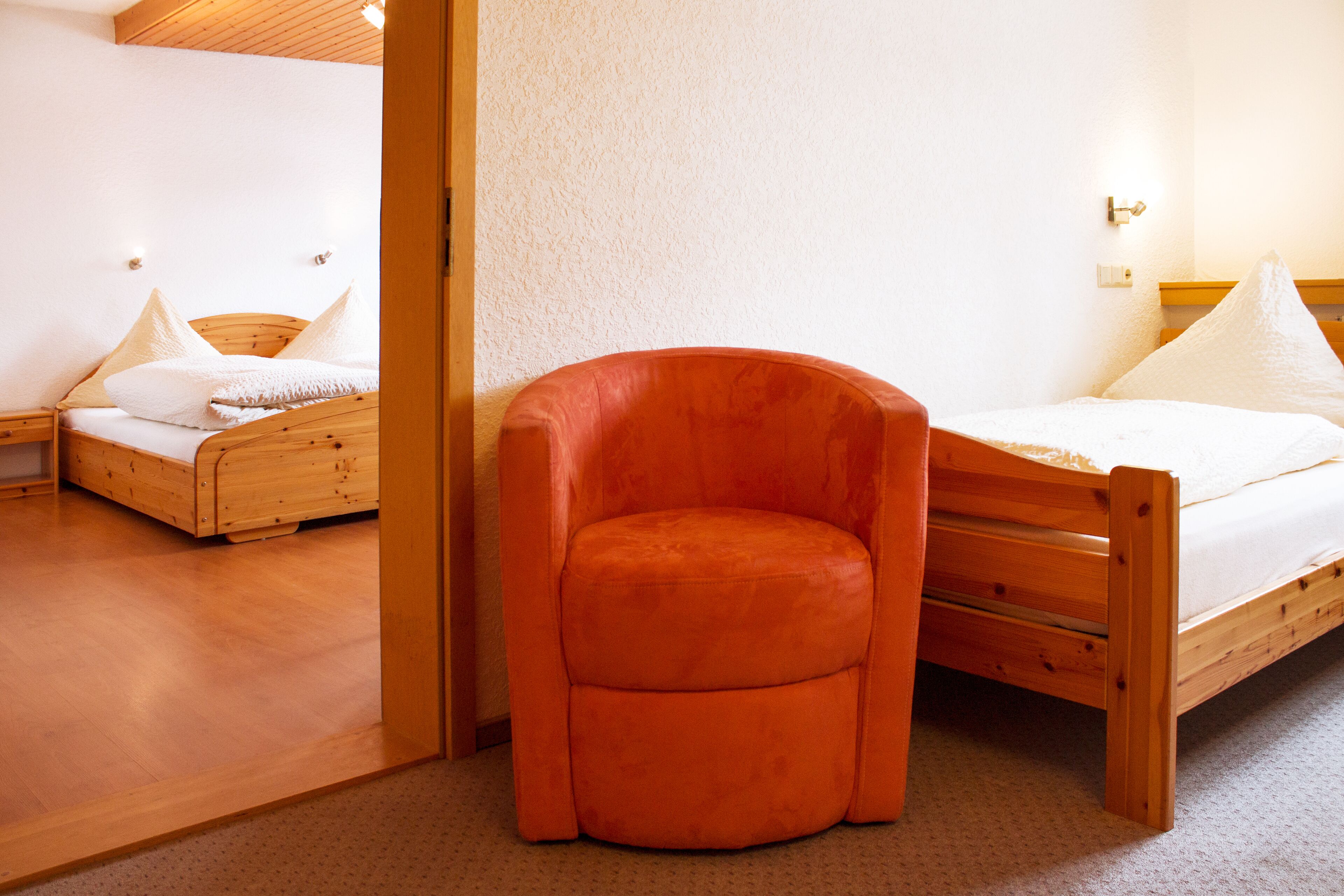A room with a wooden bed, a small orange chair, and a wooden nightstand.