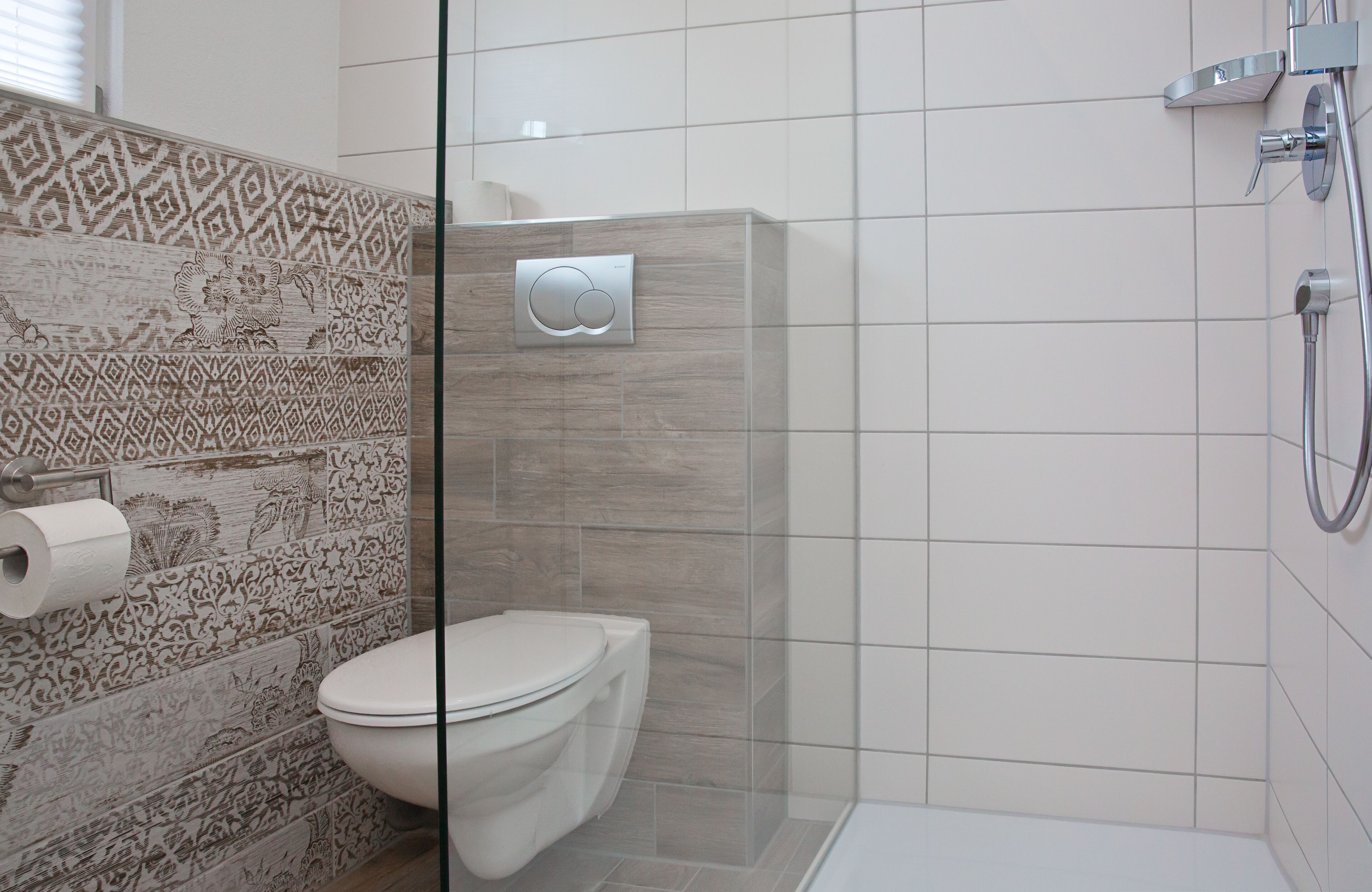A modern bathroom with a toilet, shower, and patterned wall tiles.