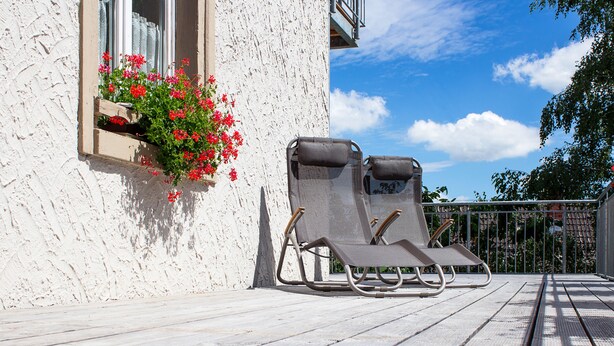 A balcony with two sun loungers and a window with red flowers. - Pension Kramer (Grafenhausen)