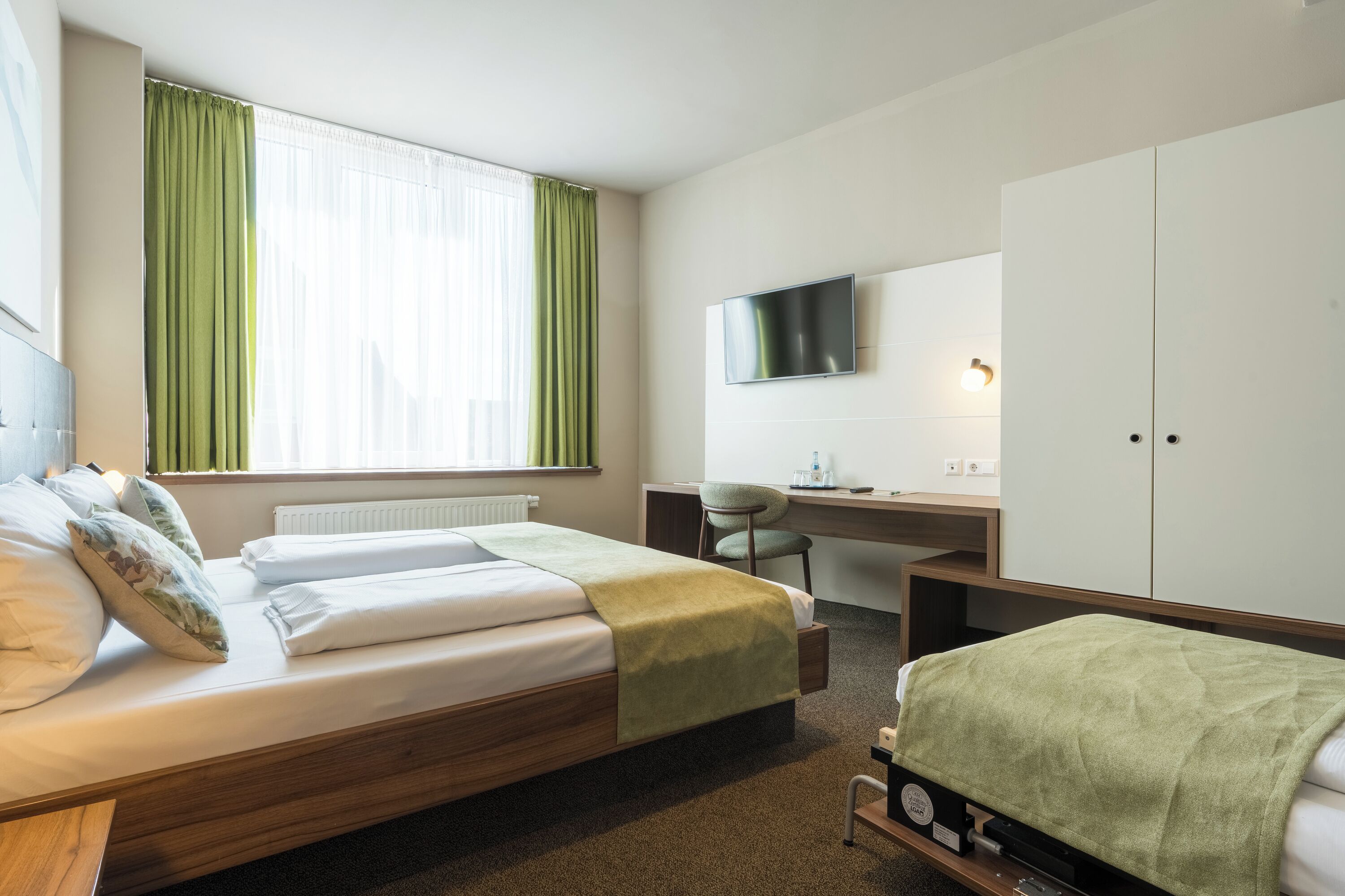A hotel room with a bed, a desk, a chair, a TV, and a wardrobe.