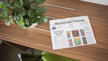 A newspaper on a wooden table with a plant beside it.