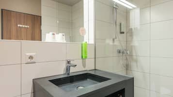 Ein Badezimmer mit Waschbecken, Spiegel, Dusche und Handtuchhalter.