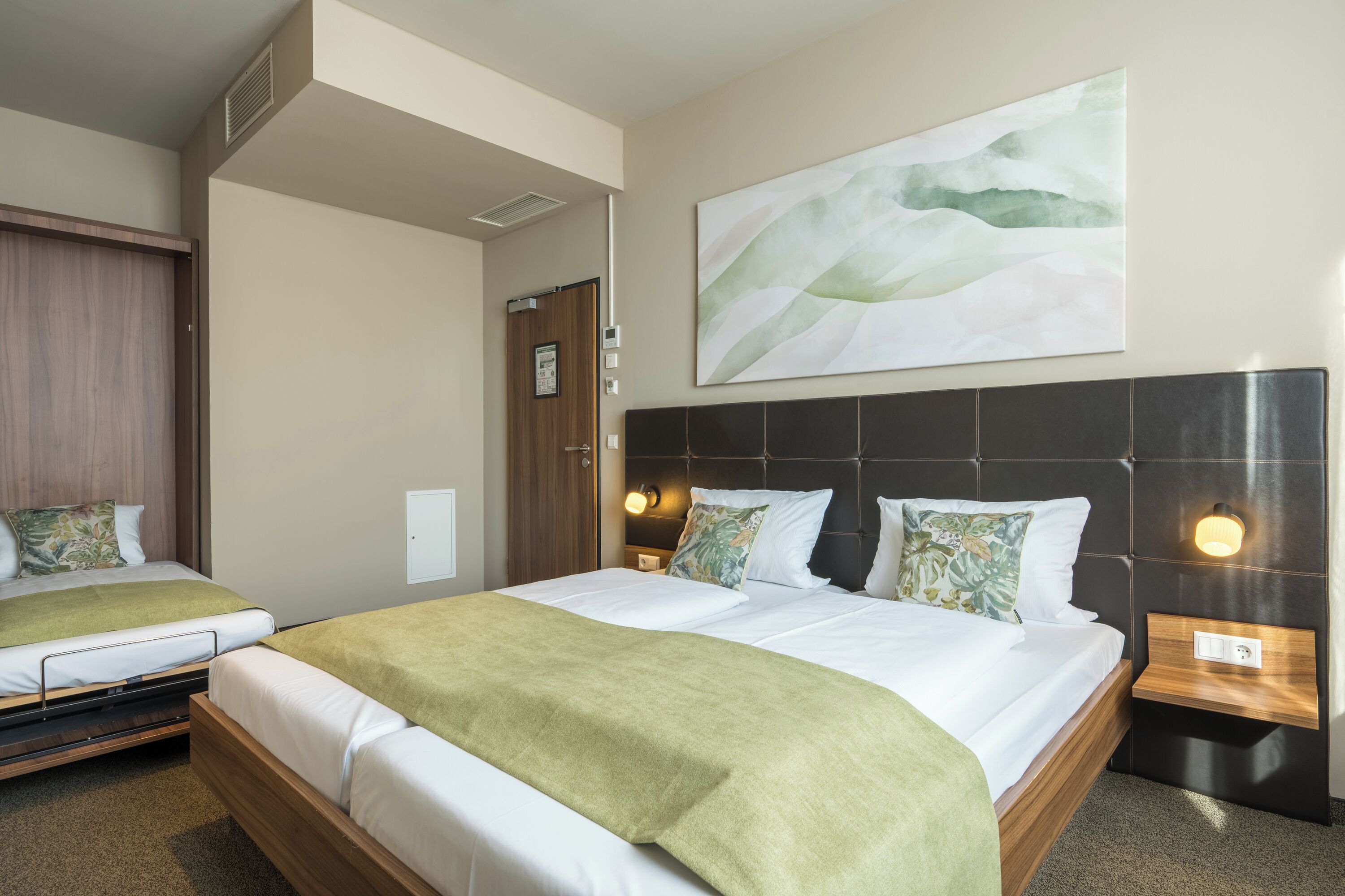 Ein Hotelzimmer mit zwei Betten, einem großen abstrakten Gemälde, einem hölzernen Kopfteil und Nachttischlampen.