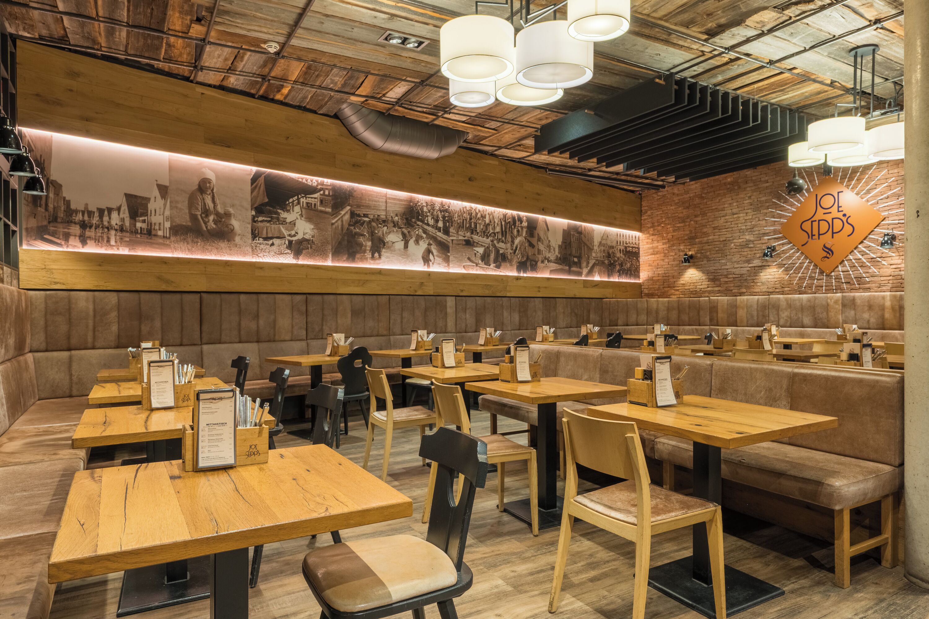Un interior de restaurante con mesas de madera, cabinas acolchadas y un menú expuesto en la pared.