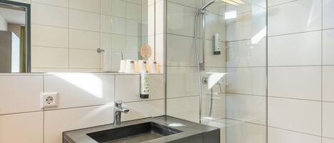 Un baño moderno con ducha de vidrio, lavamanos con espejo y toallero.