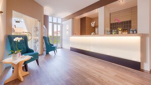 Un espace d’accueil moderne, doté d’un comptoir de réception en bois, de fauteuils turquoise et d’une grande fenêtre offrant une vue sur l’extérieur.