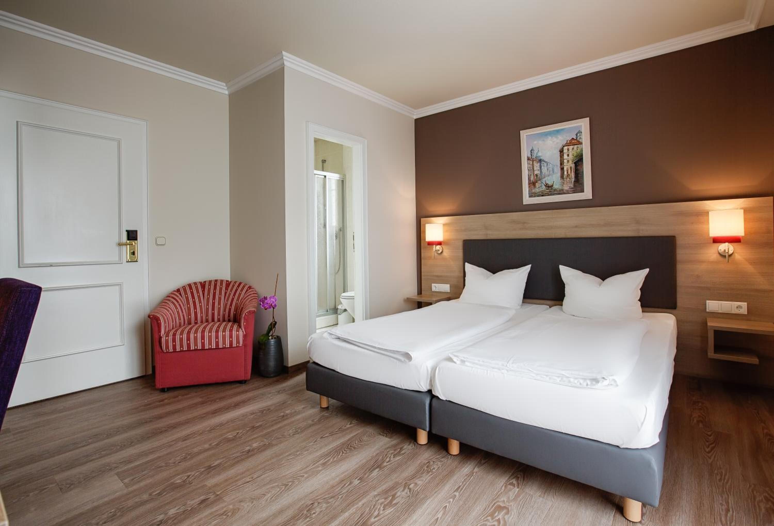 Une chambre d’hôtel avec un lit double, un fauteuil rouge et un plancher en bois.
