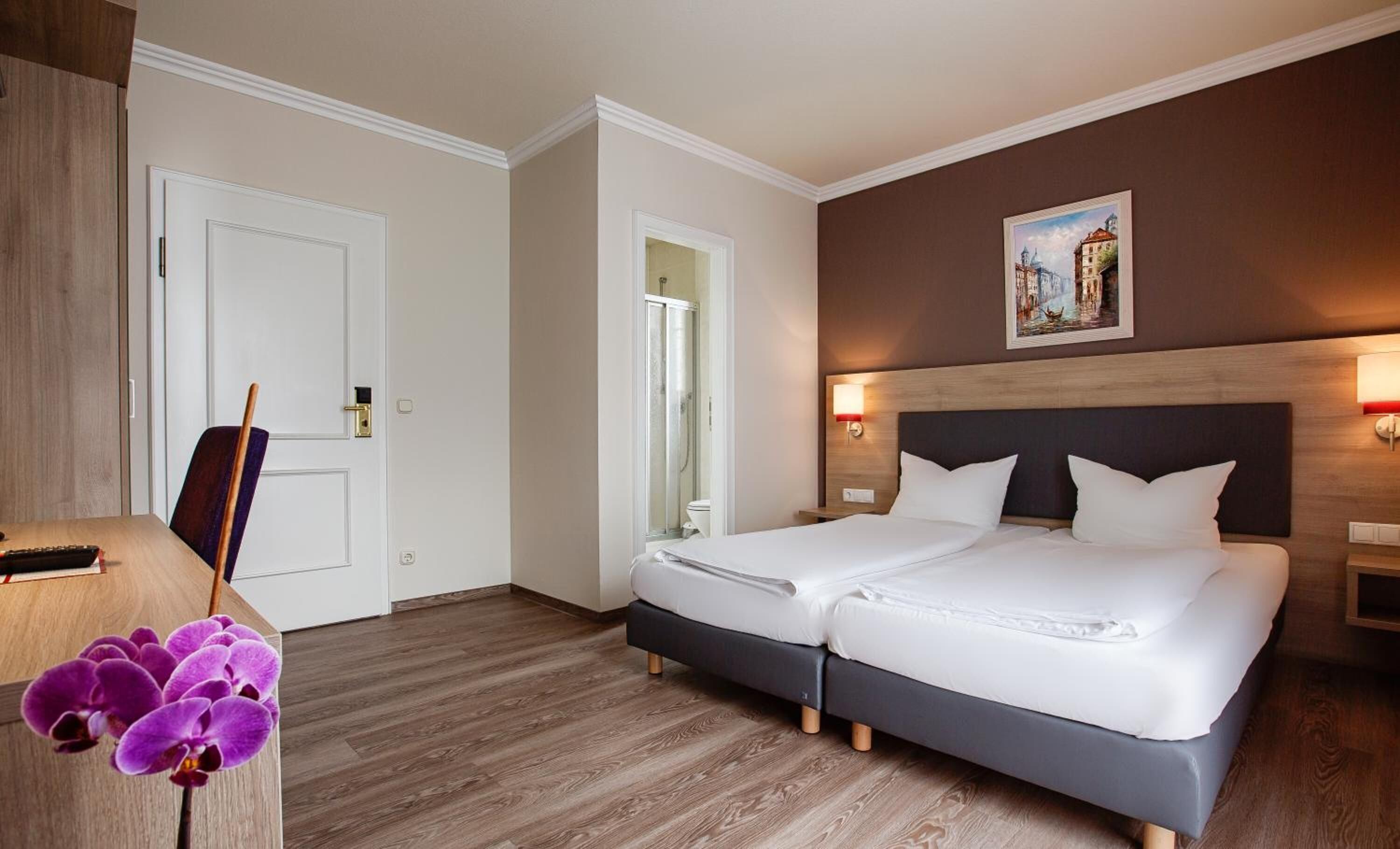 A hotel room with a double bed, a shower, and a desk with a chair.