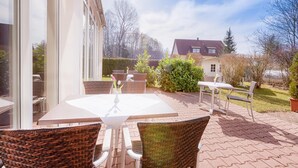 Un espace extérieur aménagé en terrasse, avec une table et des chaises, une haie et une maison en arrière-plan.